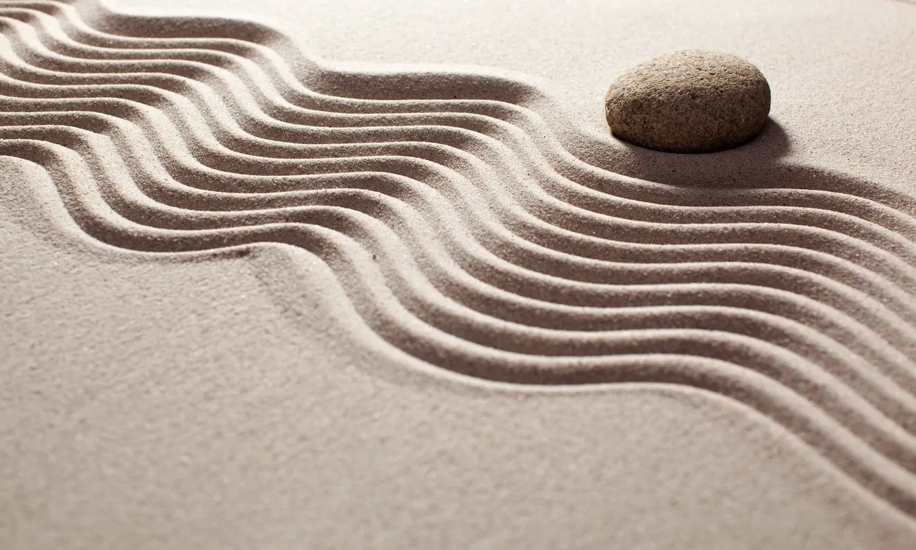 zen sand garden with pattern in the sand and a stone