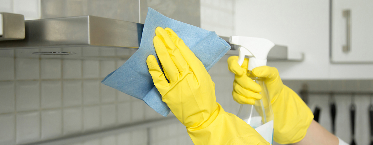 woman in rubber gloves with spray bottle cleaning stainless steel hood exhast