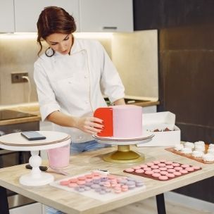focused female pastry chef in uniform preparing cake and macarons in modern kitchen