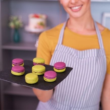 young aproned baker smiling broadly after baking tray of bright macarons
